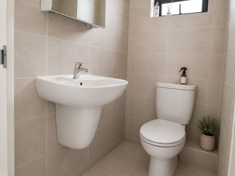 A clean, modern bathroom featuring a wall-mounted basin, a standard toilet, and neutral floor-to-ceiling tiling.