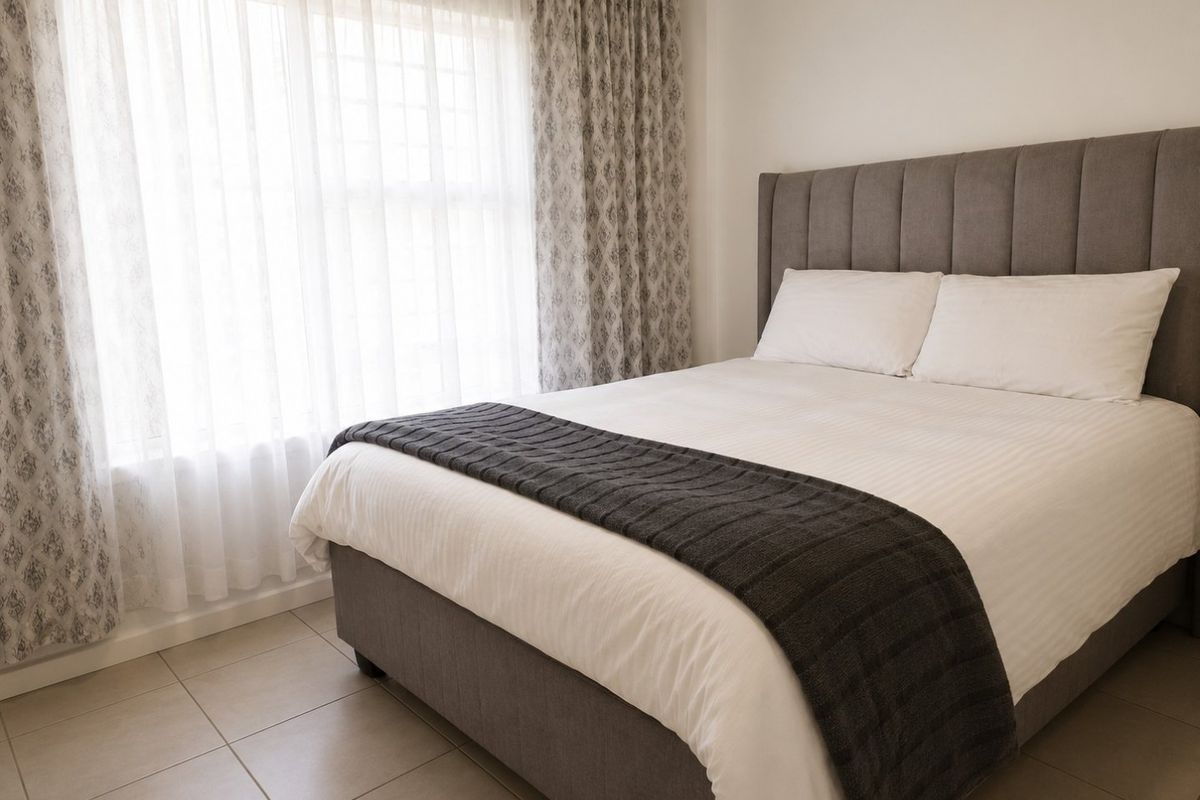 A well-maintained bedroom featuring neutral tiled flooring and large windows with installed curtain tracks, providing a bright and comfortable living space.