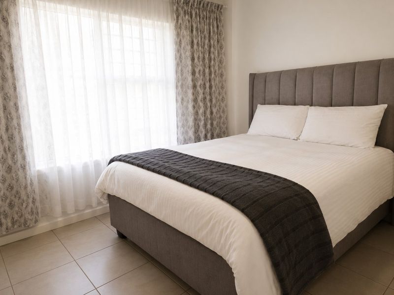 A well-maintained bedroom featuring neutral tiled flooring and large windows with installed curtain tracks, providing a bright and comfortable living space.