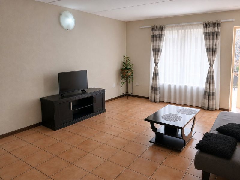 A spacious living room featuring neutral wall tones and durable ceramic tile flooring, offering a clean and functional layout with natural light.