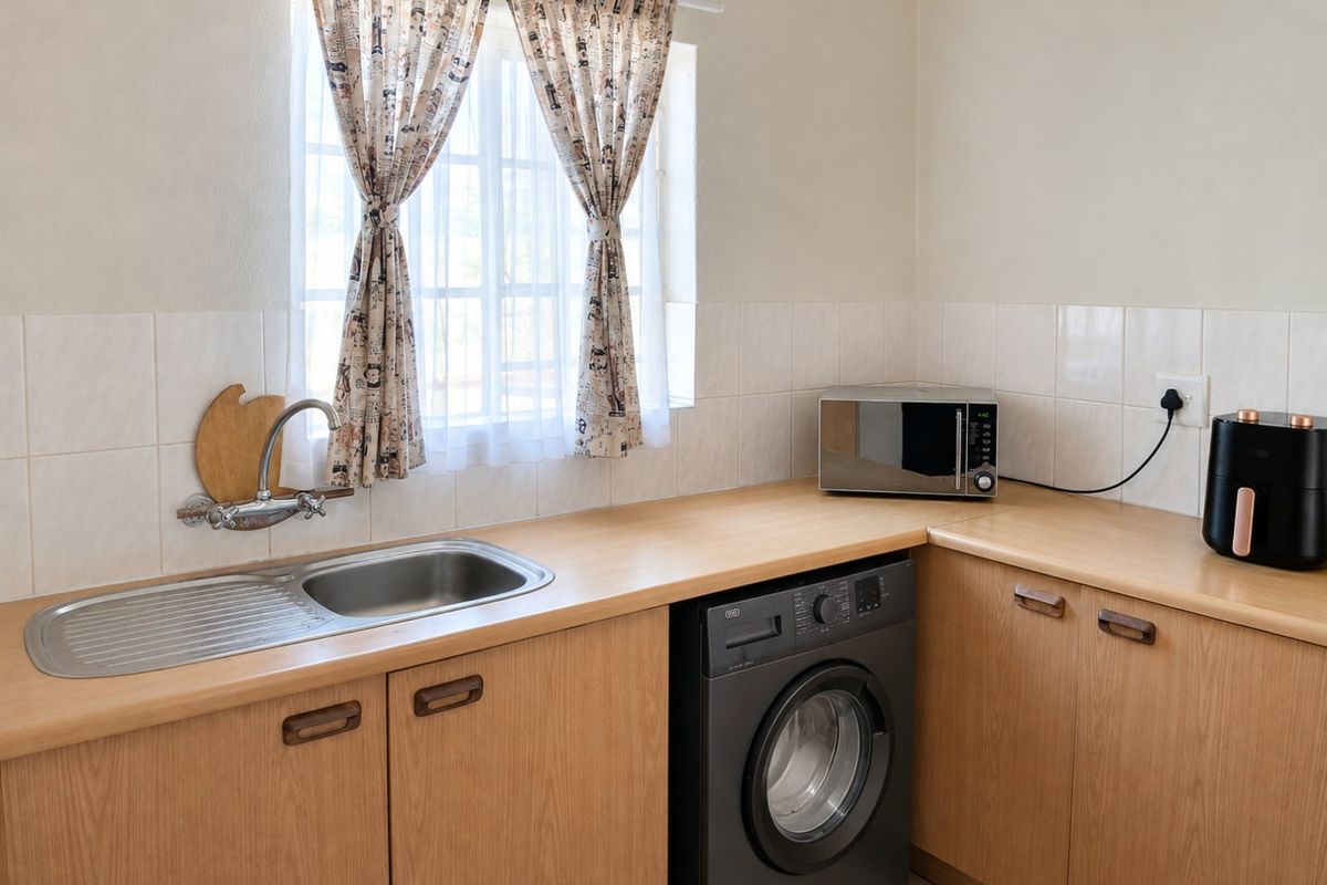 A functional laundry area featuring laminate countertops, built-in wooden cabinetry, a stainless steel sink, and tiled splashback.