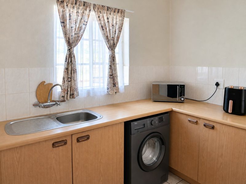 A functional laundry area featuring laminate countertops, built-in wooden cabinetry, a stainless steel sink, and tiled splashback.