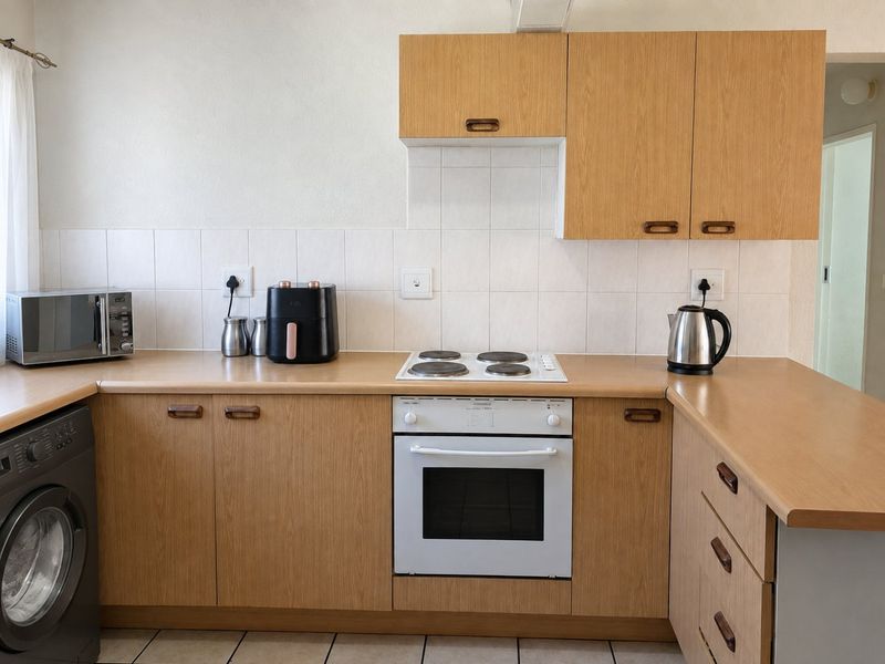A functional kitchen featuring light wood-look cabinetry, laminate countertops, a tiled backsplash, and a built-in electric oven with a hob.
