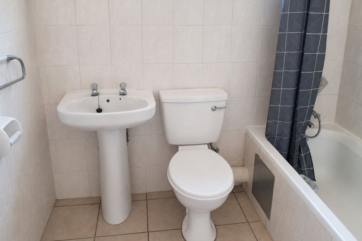 A functional bathroom featuring a pedestal basin, toilet, and bathtub with tiled walls and flooring.