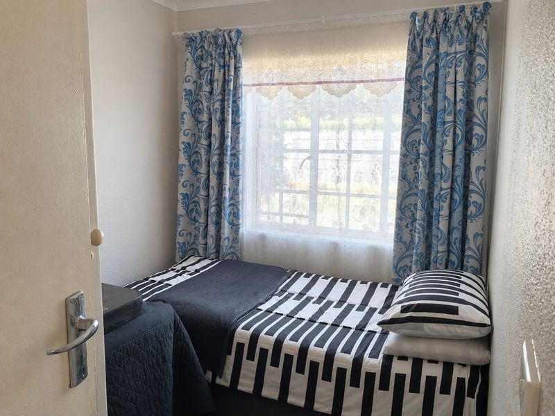 A compact bedroom featuring a window with security bars and a standard internal door.