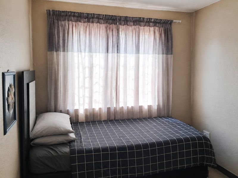A simple bedroom featuring neutral wall tones and a window with installed curtain rod, providing a functional and cozy sleeping space.