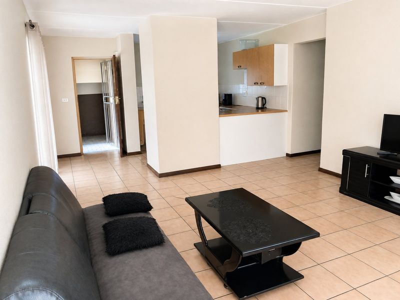 Open plan living area featuring tiled flooring and a functional kitchen with built-in cabinetry and laminate countertops, leading to a secure entrance.