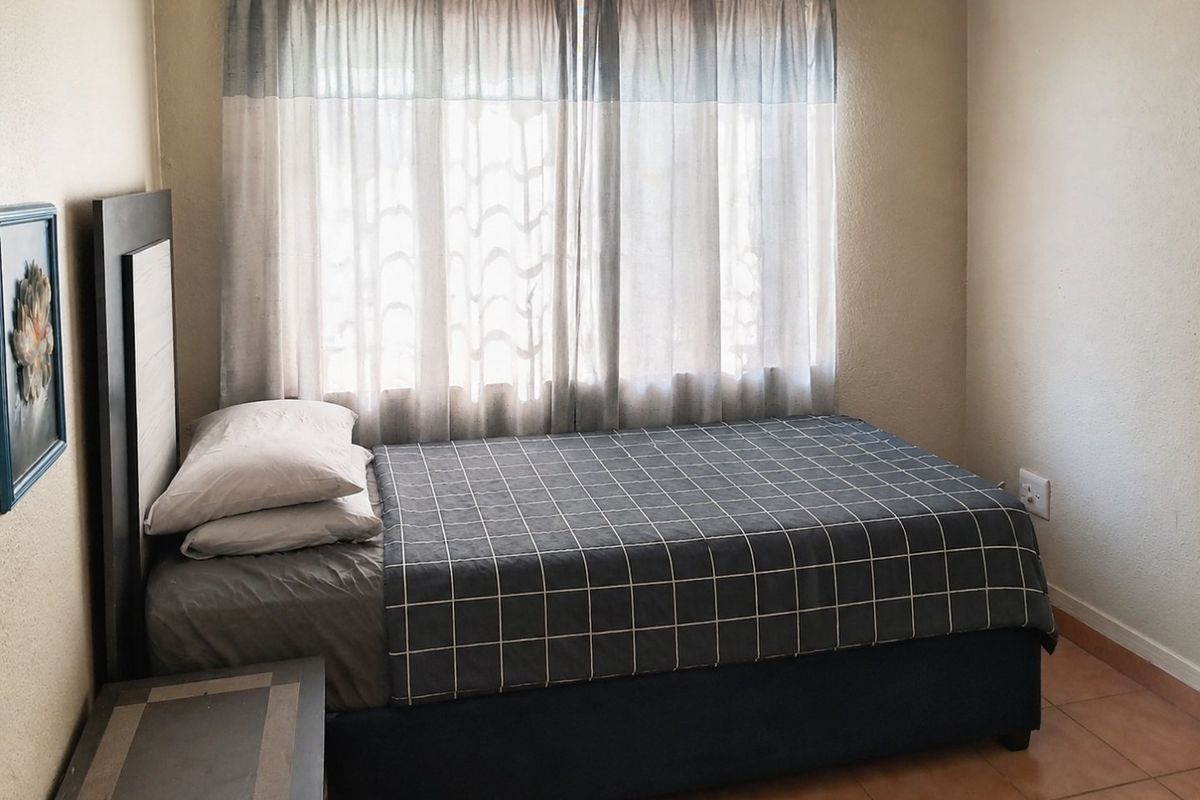 A functional bedroom featuring tiled flooring and a window with a curtain rod, providing a neutral space ready for personalization.