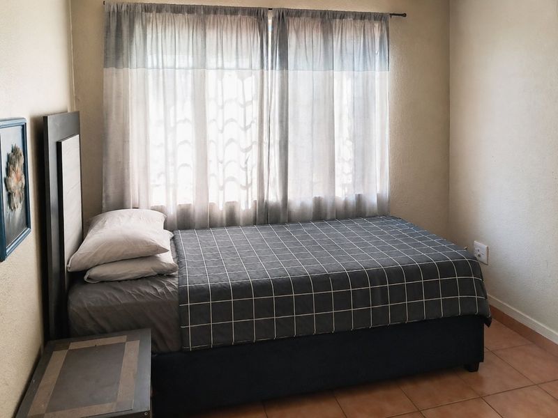 A functional bedroom featuring tiled flooring and a window with a curtain rod, providing a neutral space ready for personalization.