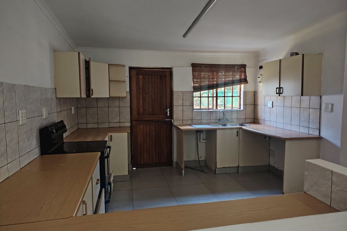 A functional kitchen featuring built-in cabinetry, laminate countertops, a double bowl sink, and a freestanding stove, with tiled splashbacks and flooring throughout.