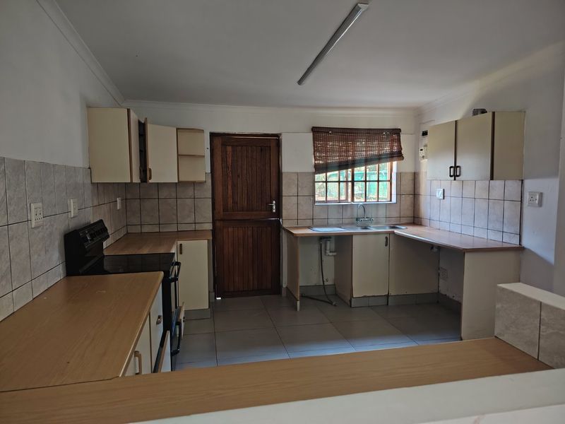 A functional kitchen featuring built-in cabinetry, laminate countertops, a double bowl sink, and a freestanding stove, with tiled splashbacks and flooring throughout.