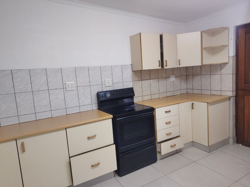 A functional kitchen featuring light-toned cabinetry, laminate countertops, a tiled backsplash, and a freestanding stove with tiled flooring.