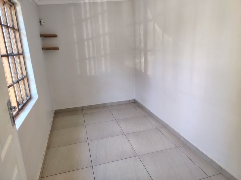 An empty bedroom featuring tiled flooring, a window with security bars, and built-in wall shelving.