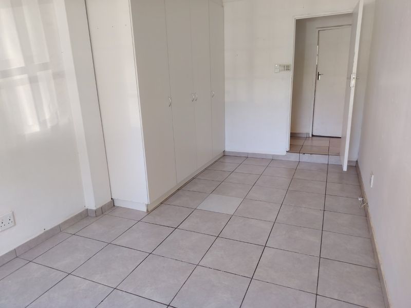 An empty bedroom featuring neutral tiled flooring and built-in white cupboards, offering a clean and versatile space ready for personalization.