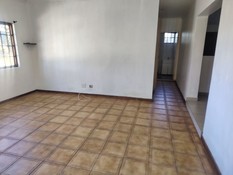 An empty living room featuring ceramic tile flooring, security bars on the window, and direct access to an adjacent hallway and bathroom area.