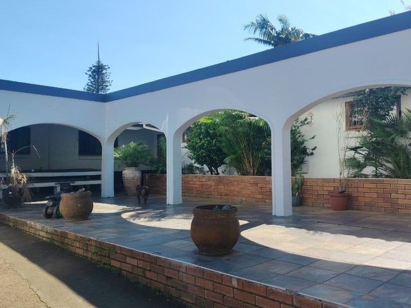 A spacious covered patio area featuring arched architectural details, tiled flooring, and a low brick retaining wall, ideal for outdoor entertaining.