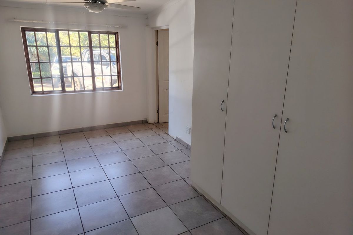 A bright, empty bedroom featuring neutral tiled flooring, built-in storage cupboards, and a ceiling fan, offering a clean canvas for personalization.