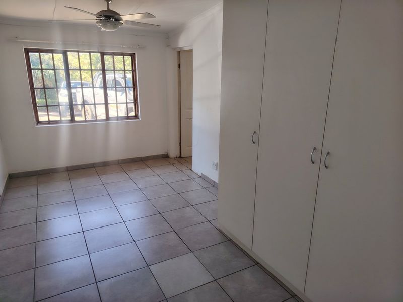 A bright, empty bedroom featuring neutral tiled flooring, built-in storage cupboards, and a ceiling fan, offering a clean canvas for personalization.