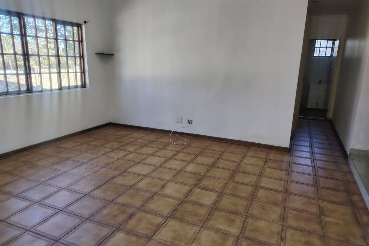 An empty living room featuring tiled flooring and a window with security bars, offering a blank canvas for interior design.