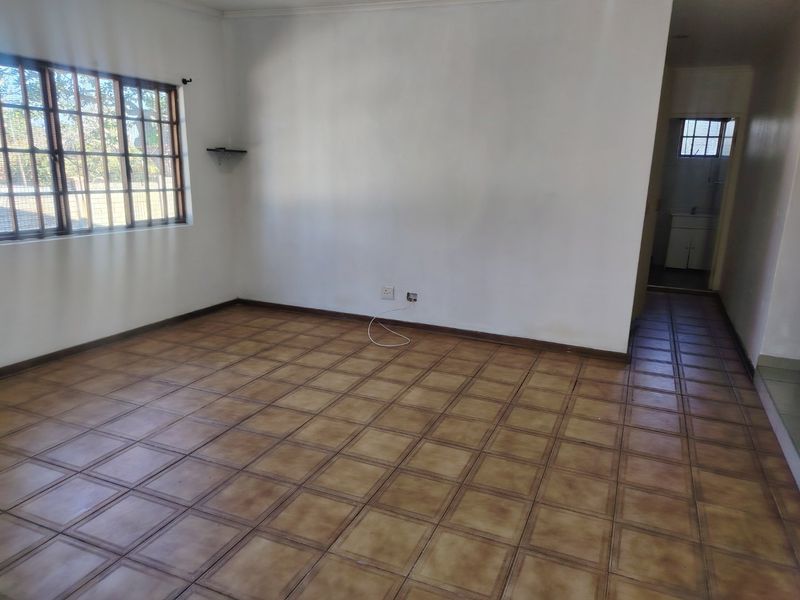 An empty living room featuring tiled flooring and a window with security bars, offering a blank canvas for interior design.