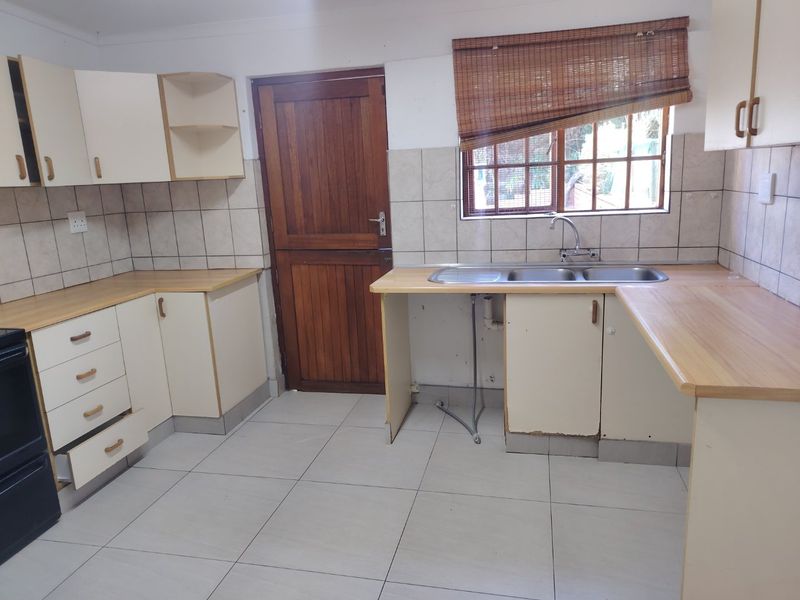 A functional kitchen featuring laminate countertops, double bowl sink, tiled splashback, and ample built-in cabinetry, ready for a modern update.