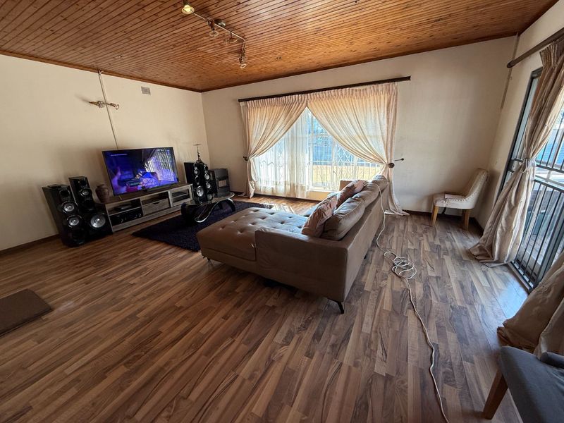 Spacious living room featuring warm timber-clad ceilings, laminate flooring, and large sliding glass doors that provide access to the exterior.