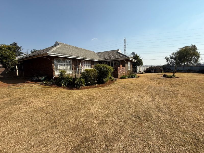 Rear view of a brick house featuring a tiled roof, a small concrete patio, and a large, dry lawn area.