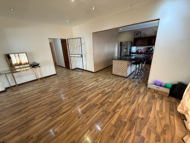 Open plan living area featuring laminate flooring and recessed lighting, flowing into a kitchen with a granite-topped island and built-in cabinetry.