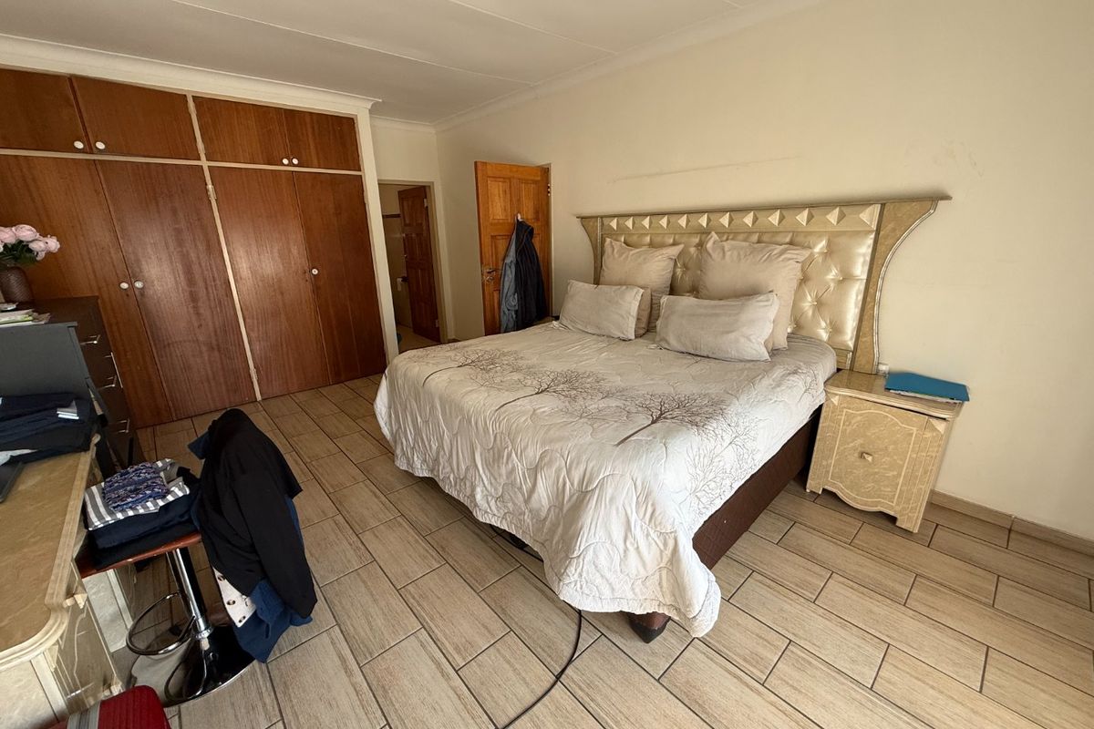 A bedroom featuring tiled flooring, built-in wooden cupboards, and a coved ceiling, offering a functional space with potential for cosmetic updates.