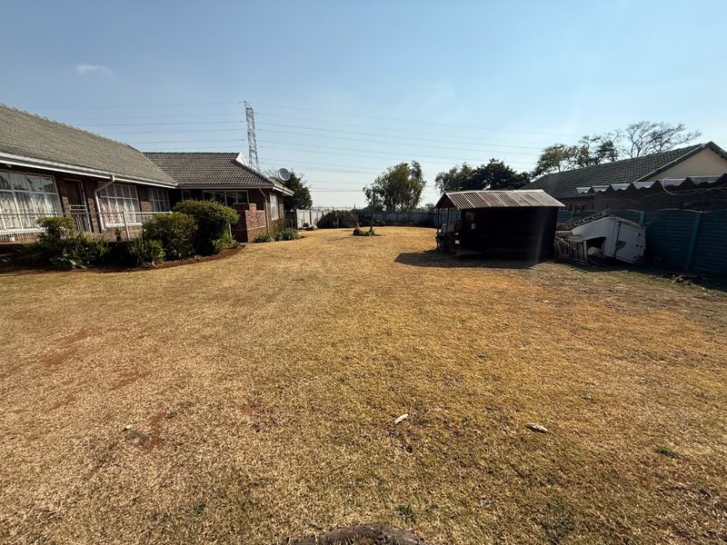 Spacious rear garden area featuring a brick house exterior, tiled roofing, and a small storage shed, offering significant potential for landscaping.