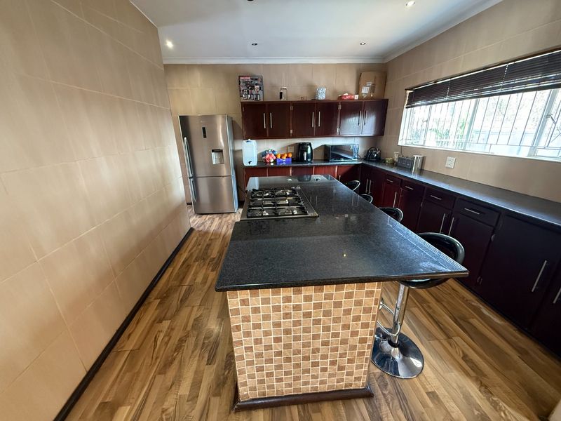 Spacious kitchen featuring dark wood cabinetry, granite countertops, a central island with a built-in gas hob, and tiled flooring.