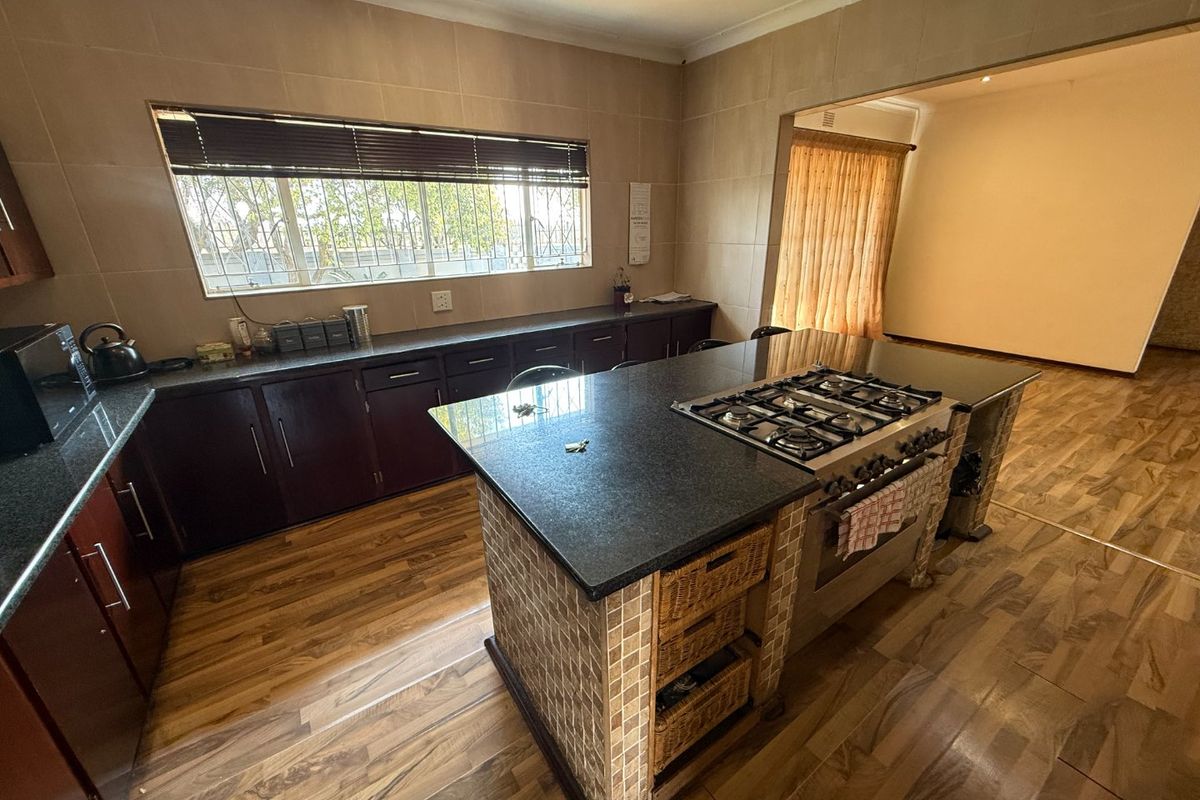 Spacious kitchen featuring dark cabinetry, granite countertops, a central island with a built-in gas hob, and tiled wall finishes.