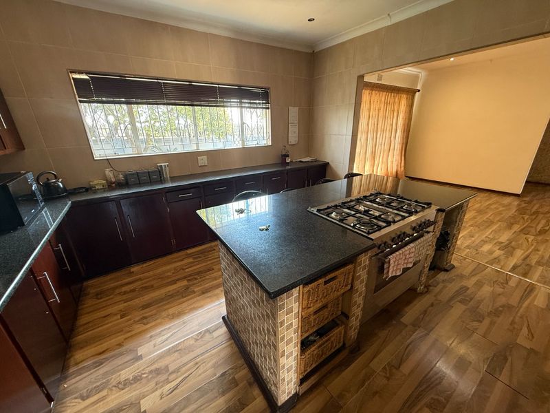 Spacious kitchen featuring dark cabinetry, granite countertops, a central island with a built-in gas hob, and tiled wall finishes.