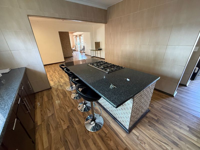 Kitchen featuring a central island with a built-in gas hob, granite countertops, and tiled wall finishes, flowing into an adjacent living area.