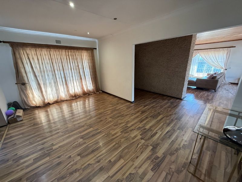 Spacious living area featuring modern laminate flooring, recessed downlighting, and a distinctive textured stone feature wall, offering a bright and open layout.
