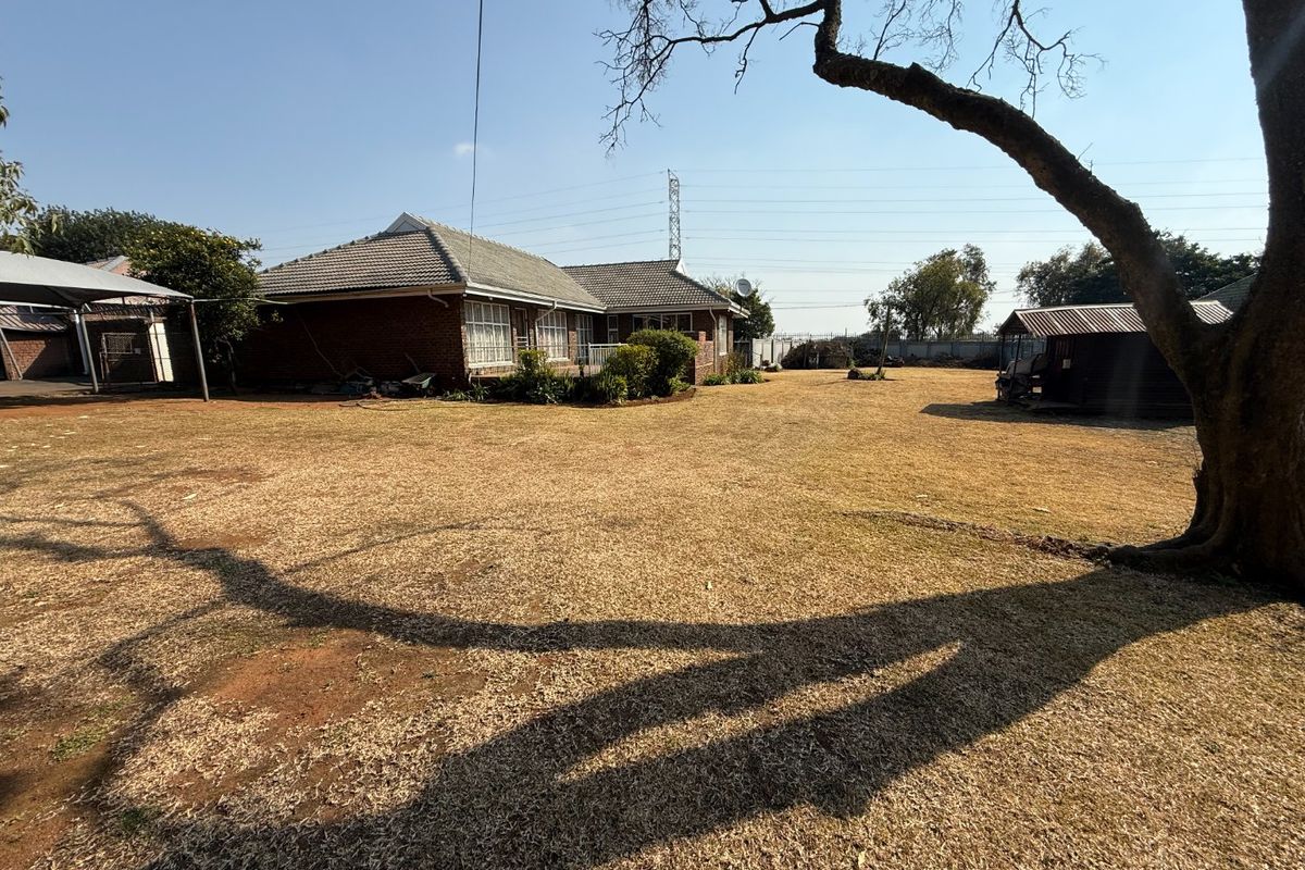 Spacious rear garden area featuring a brick house with a tiled roof, a detached carport, and an outbuilding structure.