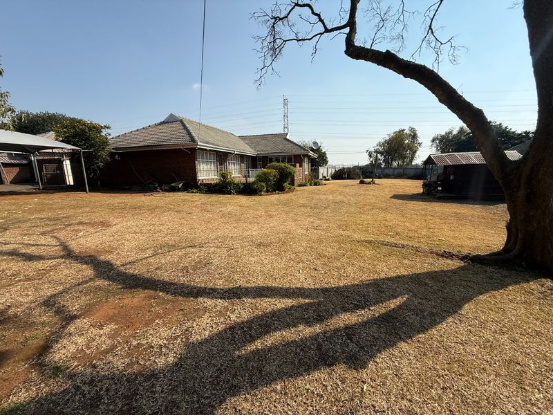 Spacious rear garden area featuring a brick house with a tiled roof, a detached carport, and an outbuilding structure.
