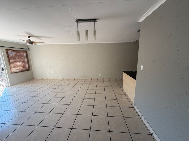 Spacious open-plan living area featuring neutral tiled flooring, a breakfast bar, and modern pendant lighting, offering a versatile layout for dining and relaxation.