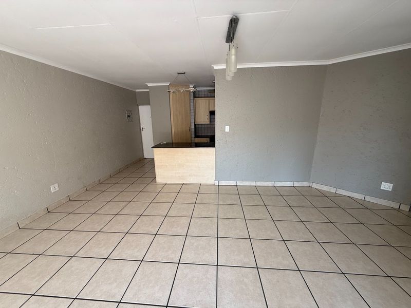 An open-plan living and kitchen area featuring tiled flooring, a breakfast bar, and neutral grey walls, offering a blank canvas for personalization.