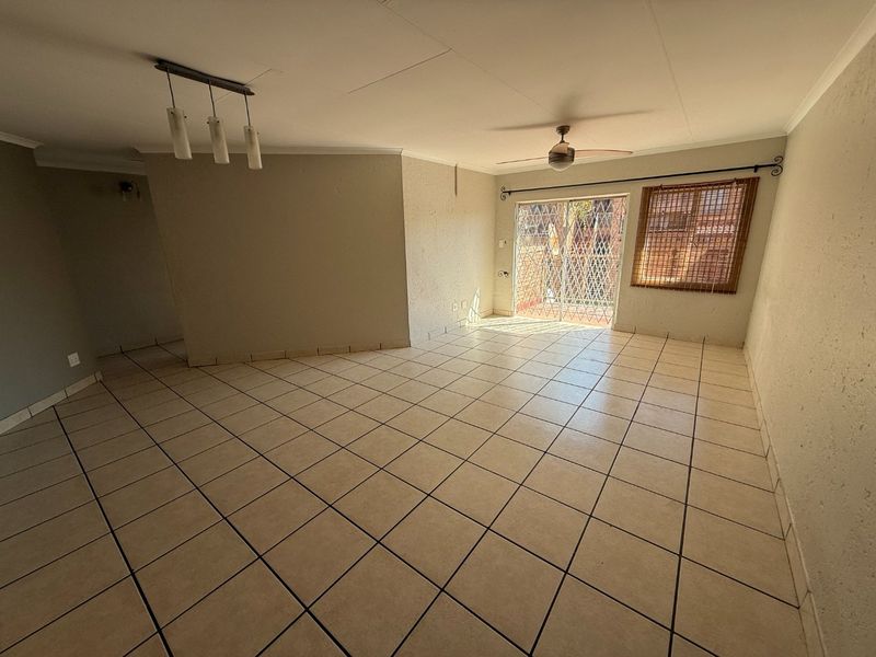 A spacious, empty living area featuring neutral tiled flooring, a ceiling fan, and a sliding glass door with security gate leading to the exterior.