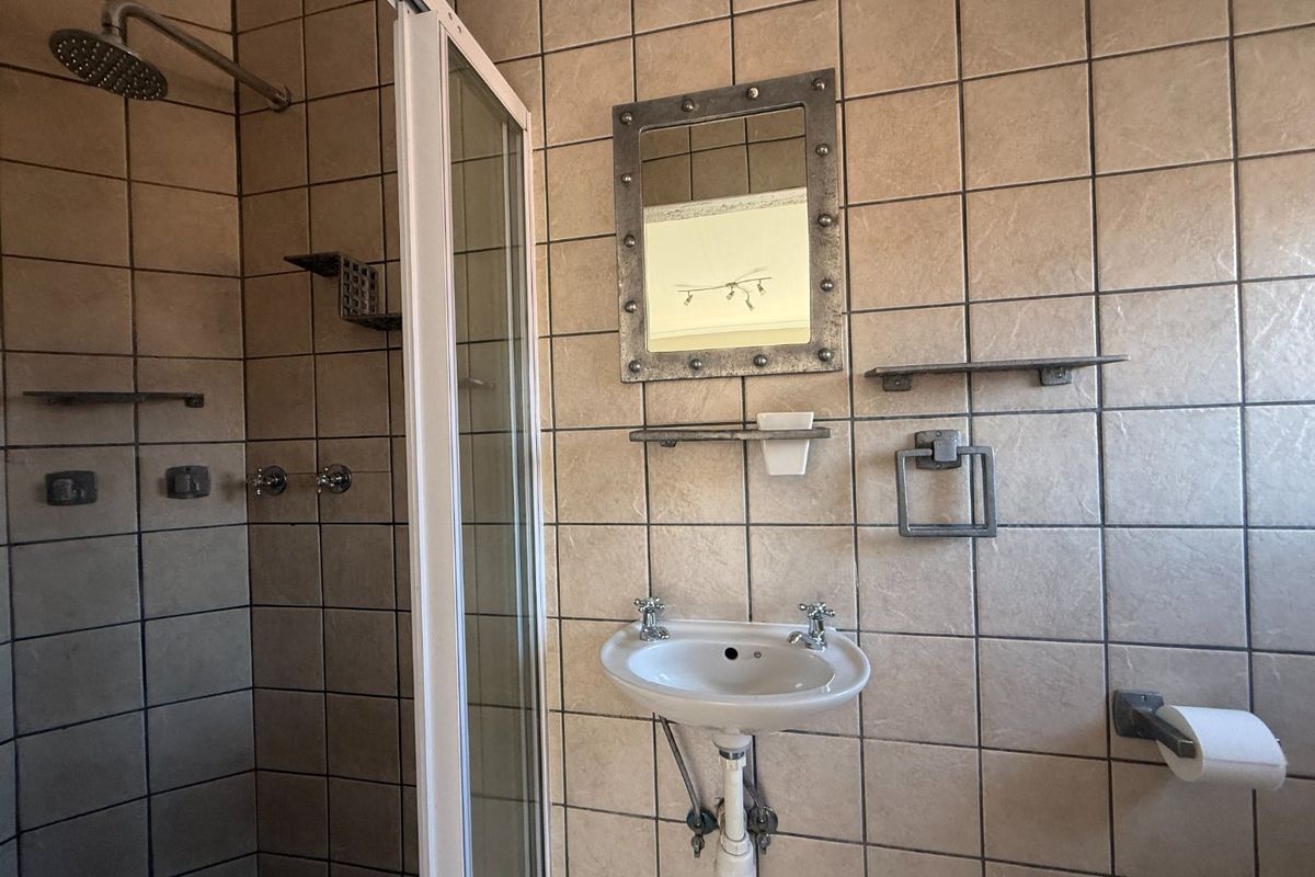 A functional bathroom featuring a shower enclosure with a rain shower head, a wall-mounted basin, and neutral wall tiling throughout.