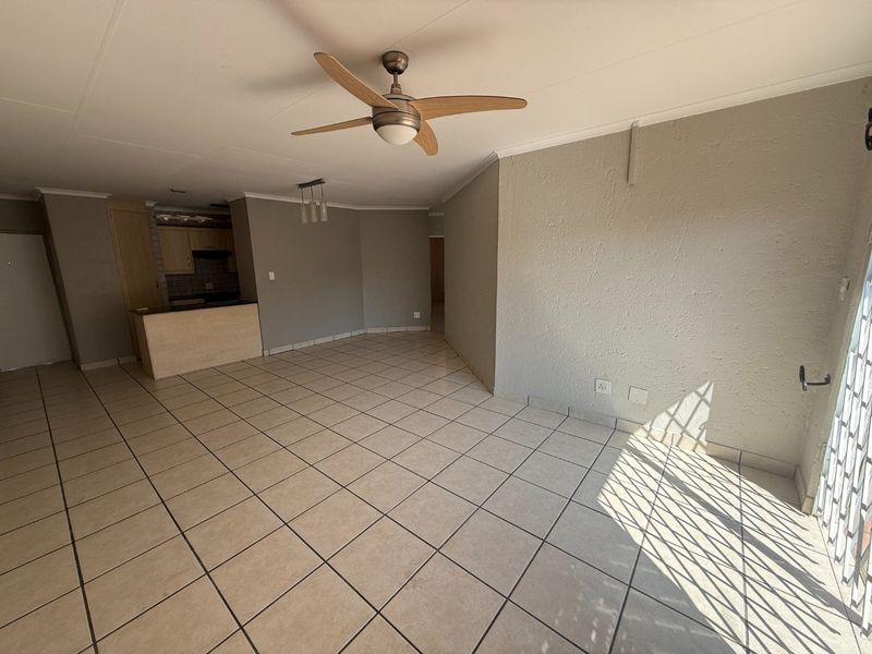An open-plan living and kitchen area featuring neutral tiled flooring, a ceiling fan, and a functional kitchen layout with built-in cabinetry.