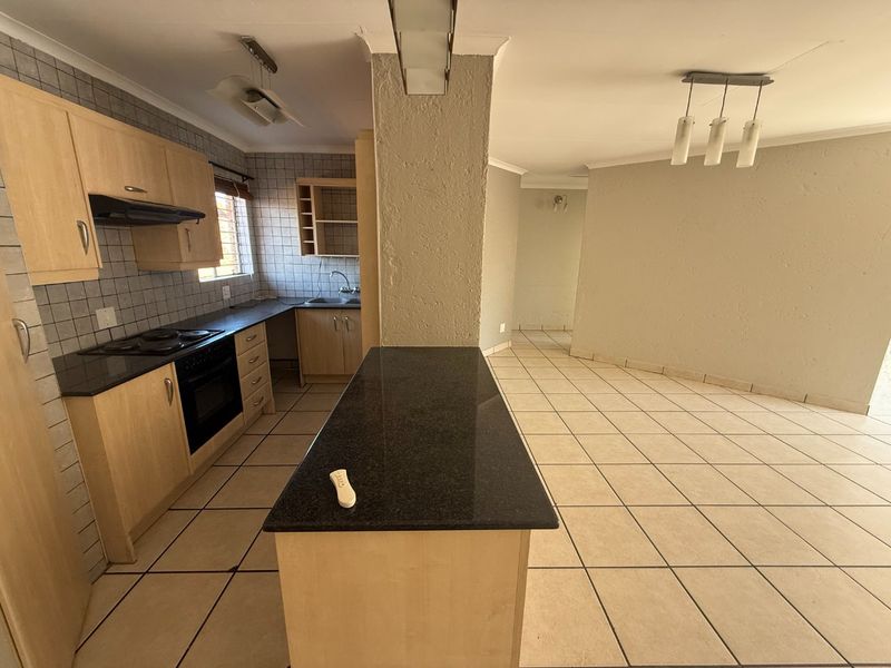 Open-plan kitchen and living area featuring light wood cabinetry, granite countertops, tiled flooring, and a central kitchen island with integrated appliances.