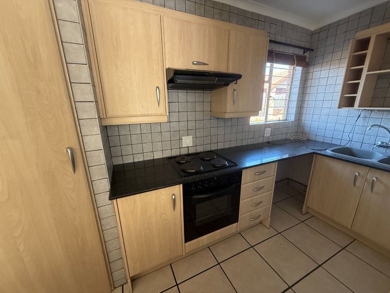 A functional kitchen featuring light wood cabinetry, dark laminate countertops, a built-in electric hob and oven, and tiled finishes throughout.