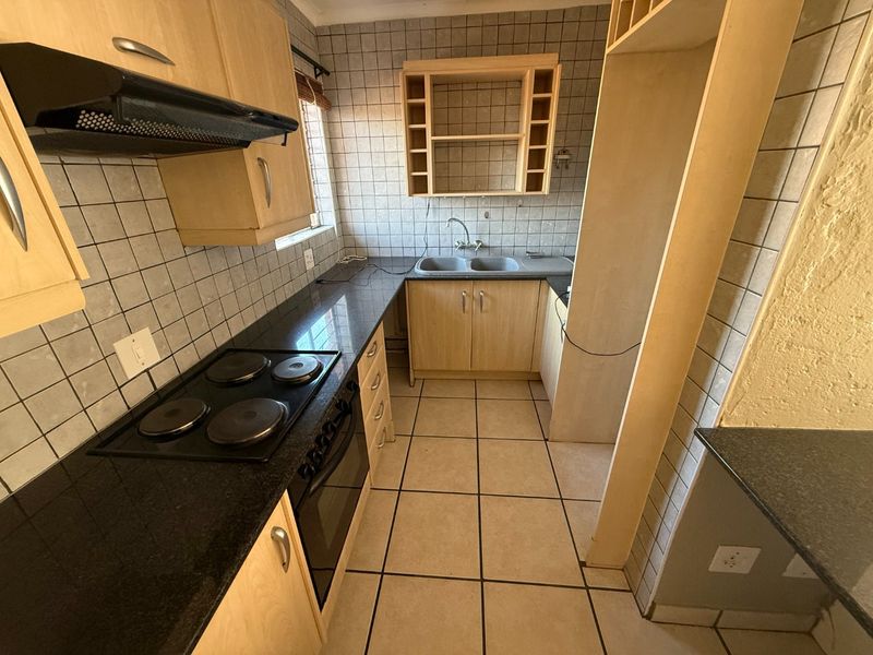 A functional kitchen featuring light wood cabinetry, granite countertops, a built-in oven and hob, and tiled finishes throughout.