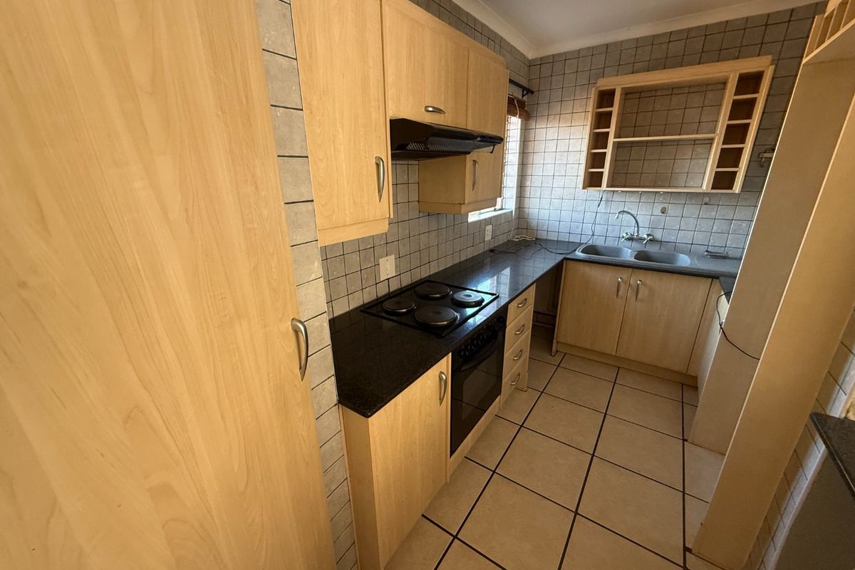 A functional kitchen featuring laminate cabinetry, granite countertops, an electric hob, built-in oven, and double bowl sink with tiled finishes throughout.