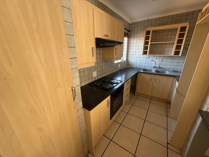 A functional kitchen featuring laminate cabinetry, granite countertops, an electric hob, built-in oven, and double bowl sink with tiled finishes throughout.