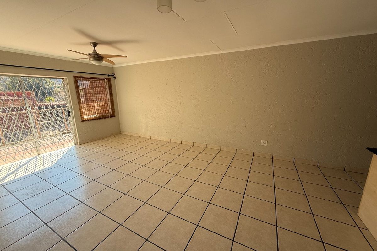An empty, open-plan living area featuring neutral tiled flooring, a ceiling fan, and a sliding glass door leading to an outdoor space.
