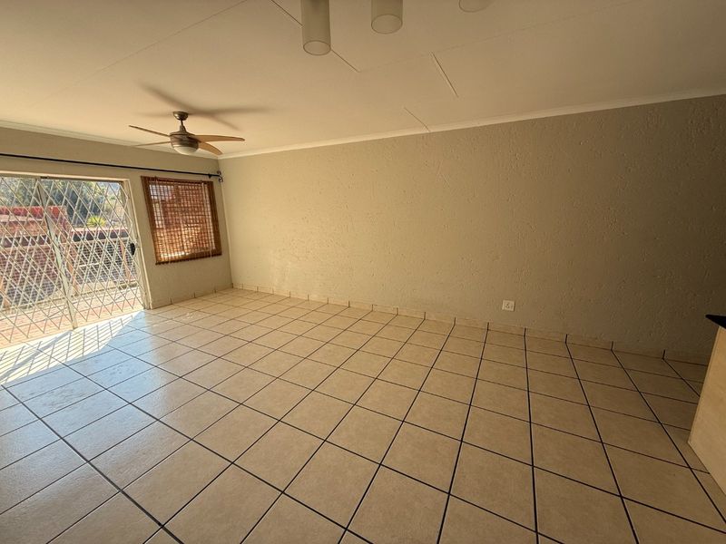An empty, open-plan living area featuring neutral tiled flooring, a ceiling fan, and a sliding glass door leading to an outdoor space.