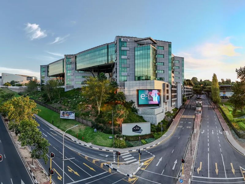Aerial view of a modern commercial office complex featuring a glass facade, integrated digital signage, and secure gated access from the main road.